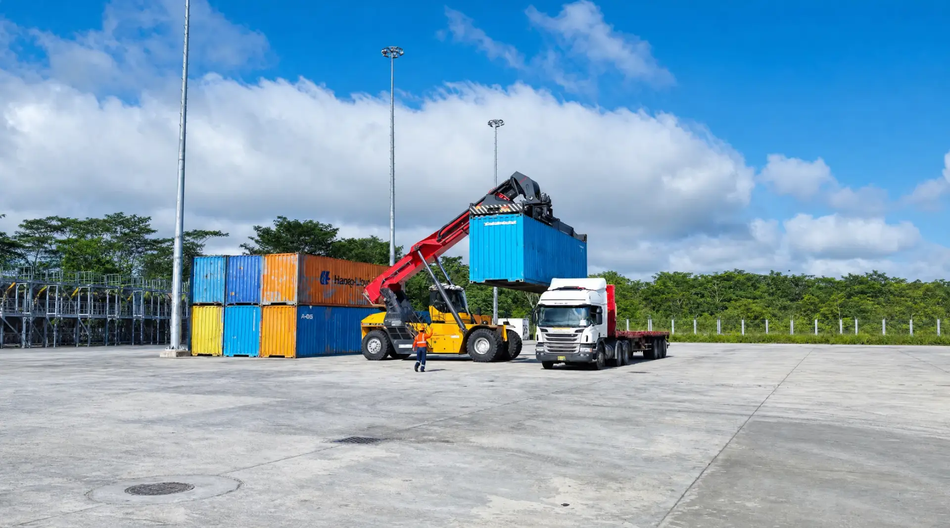 Reach stacker cargando un contenedor sobre un camión en el patio del terminal, con vegetación amazónica al fondo