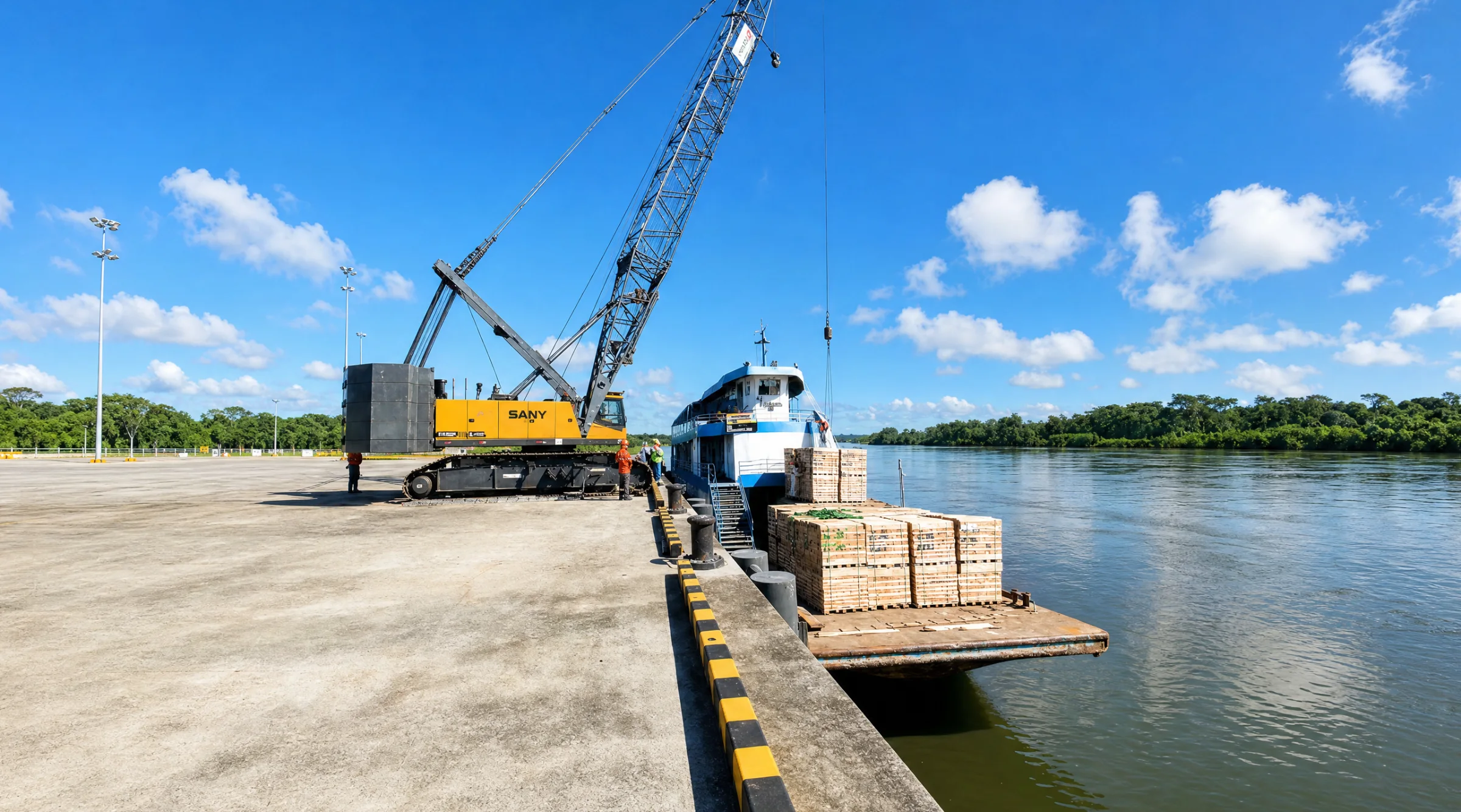 Grúa celosía en el muelle del terminal junto a una nave fluvial cargada con madera en el río Huallaga