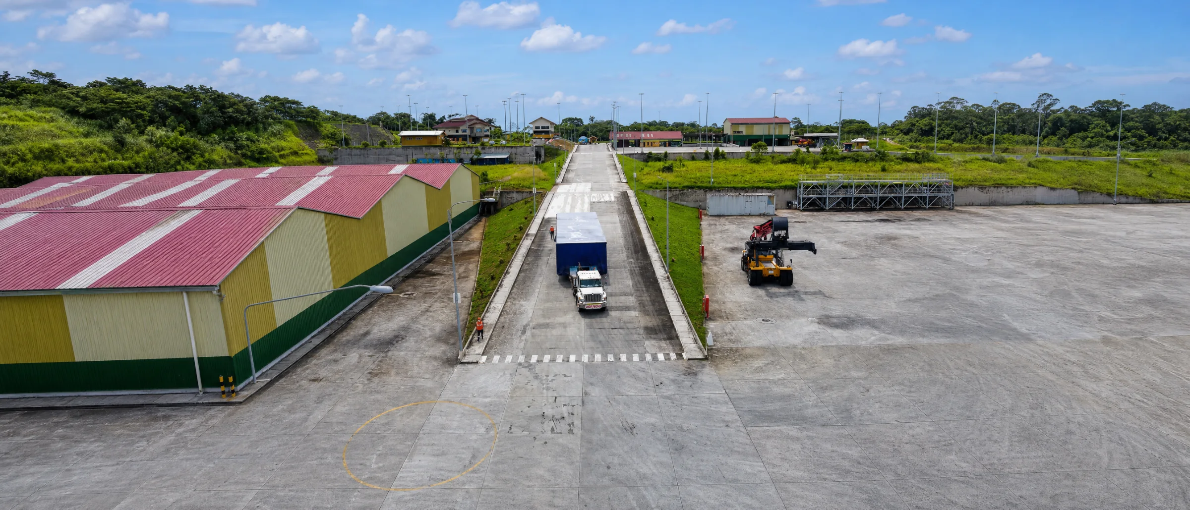 Camión con contenedor en la vía interna del terminal, junto al almacén y el patio
